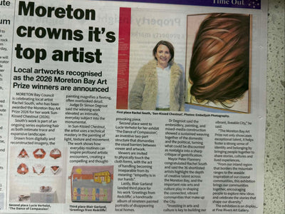 A printed newspaper page featuring a large headline about Moreton crowns it's top artist, with columns of text, small inset photos, and a close-up hair image. The page is photographed on a speckled countertop.