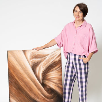 Woman standing next to a large photo of blonde hair on a white background